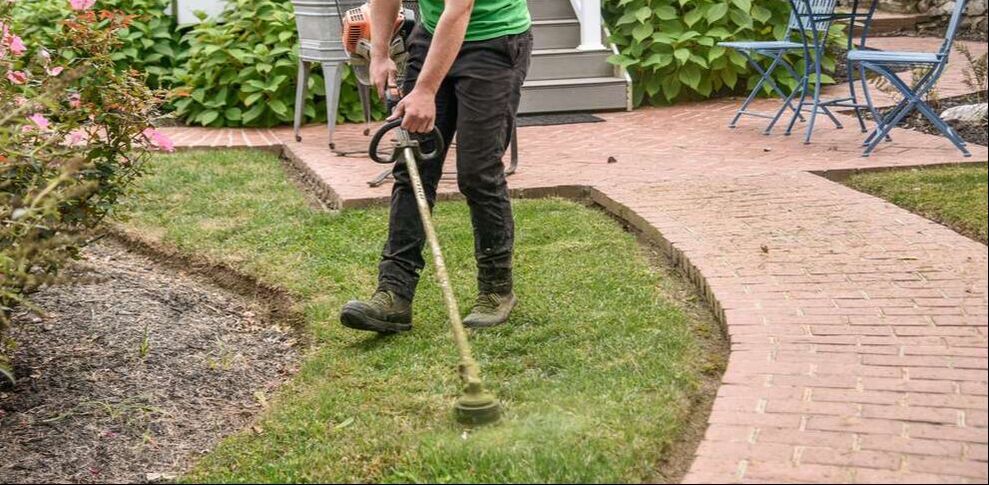 Lower half of a person with a weed eater working next to a brick pathway