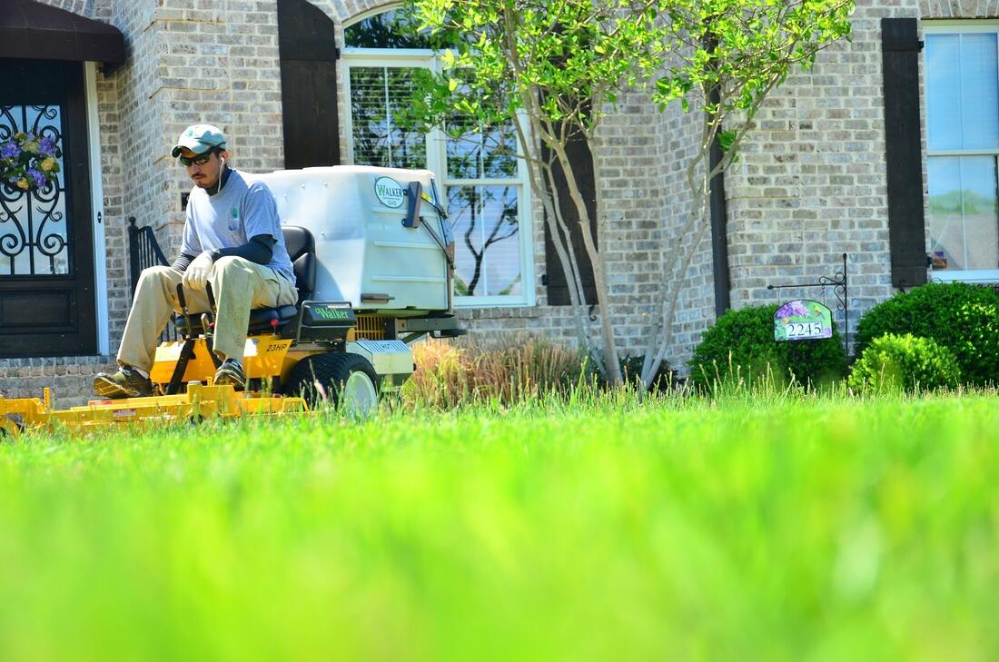 Man riding a yellow lawn mower with a brick house in background